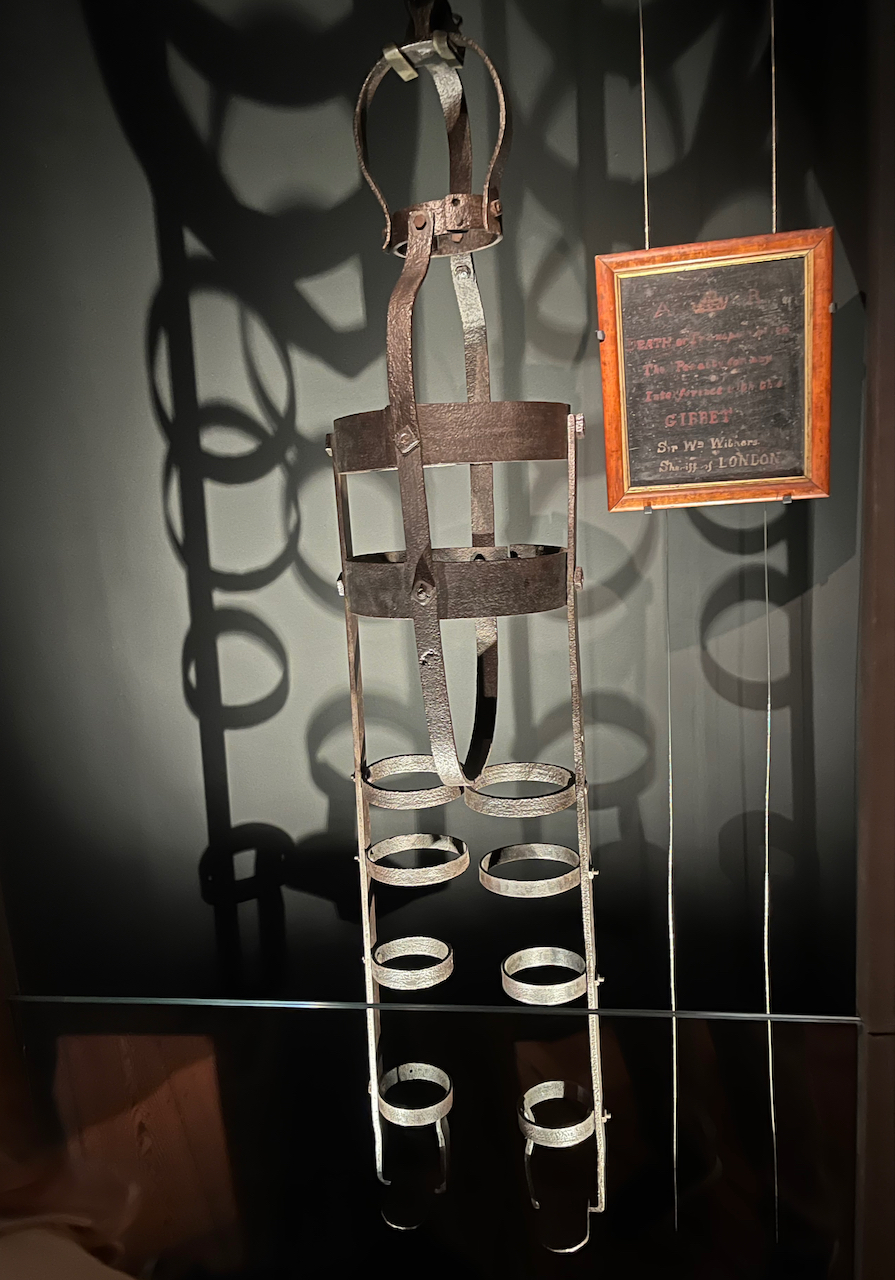 A gibbet, a tall iron cage used to hold the executed bodies of criminals. It includes 4 metal rings that fasten around each leg, 2 larger rings that go around their chest, and a ring that goes around the neck.