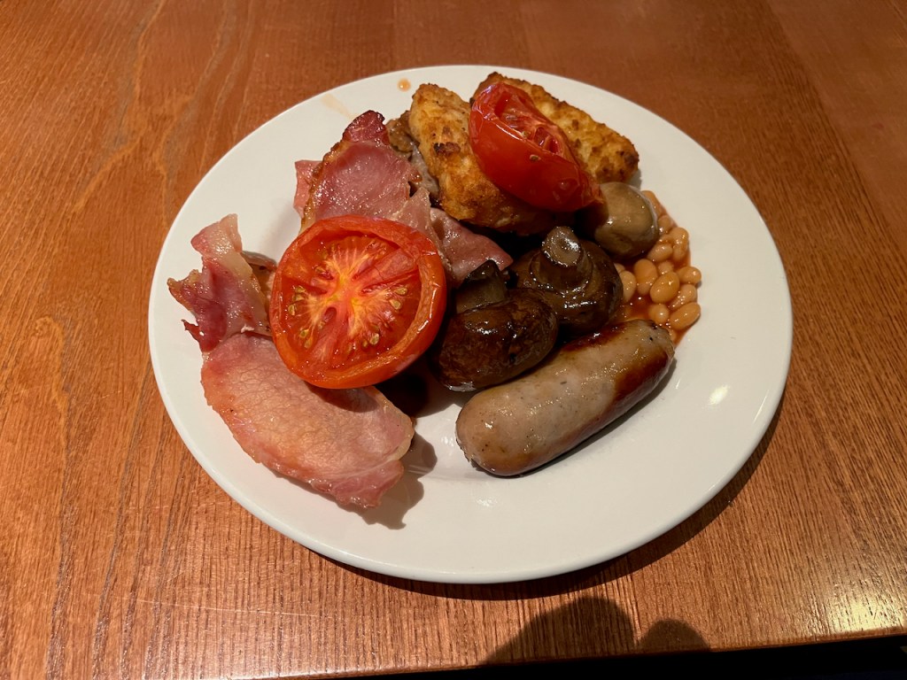 A large plate of breakfast at the Torquay premier inn, including bacon, sausages, mushrooms, tomatoes, hash browns and baked beans.