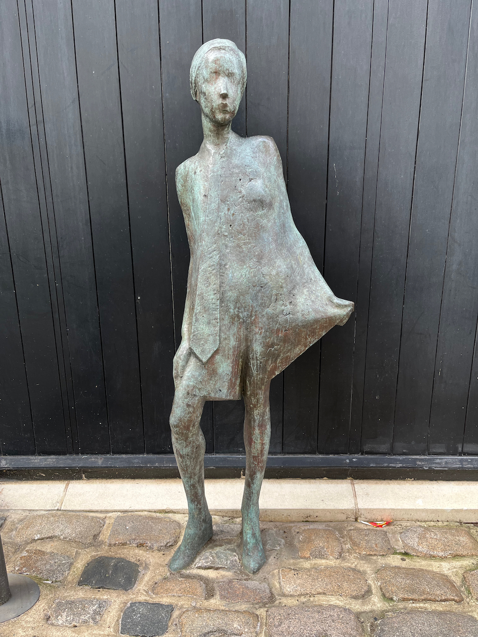 Bronze statue of fashion model Twiggy posing. She is standing with her right leg slightly bent, while holding out the left hem of her dress.