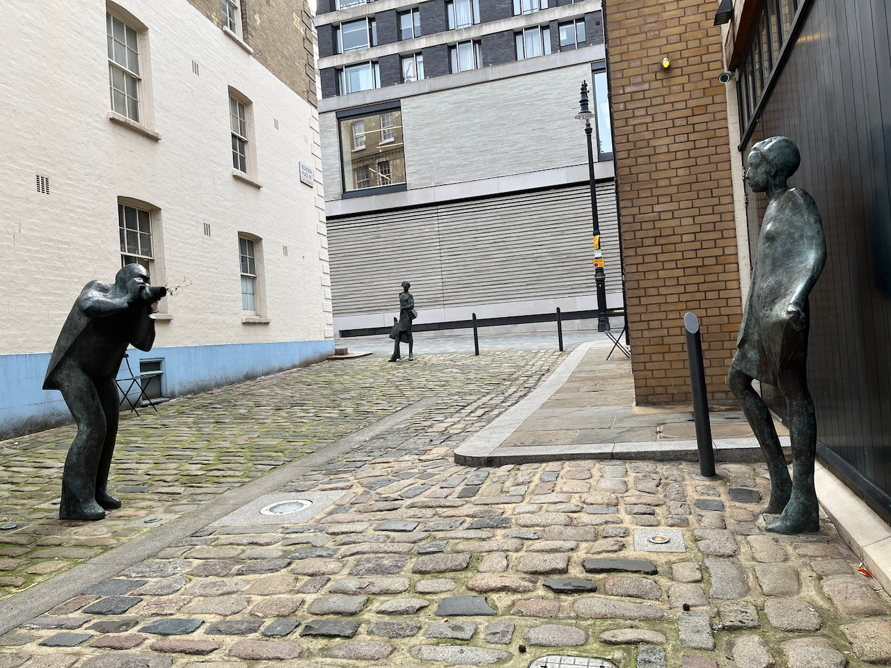 Bronze sculptures of Terence Donovan photographing Twiggy in a cobbled street, with a further statue of a female shopper stopping to look at them at the far end of the street.