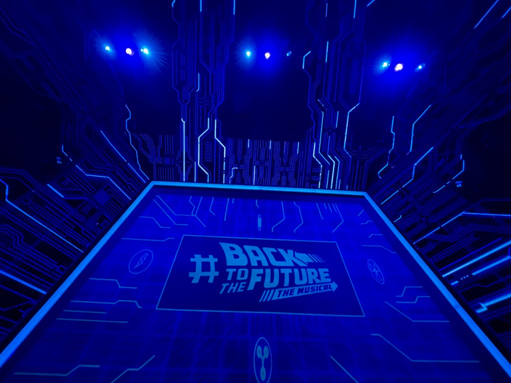 Lots of blue lines, some lit up, designed to look like electrical circuits, spreading from the top and sides of the stage across the walls and ceiling of the auditorium. The big projection screen on the stage is showing the logo for Back To The Future The Musical.