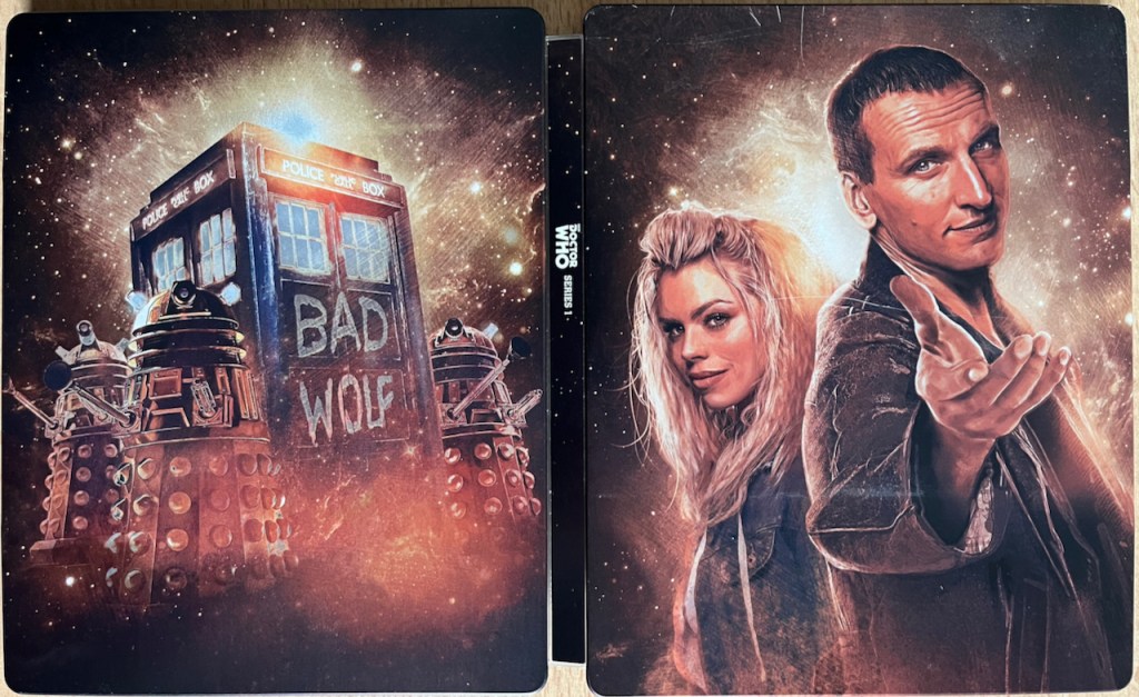 The full cover spread artwork for the Doctor Who Series 1 Blu-ray steelbook. The front cover shows the Doctor and Rose looking at us, with the Doctor reaching out his hand in a beckoning gesture. The back cover shows Daleks surrounding the Tardis, which has Bad Wolf painted in big white letters on it.