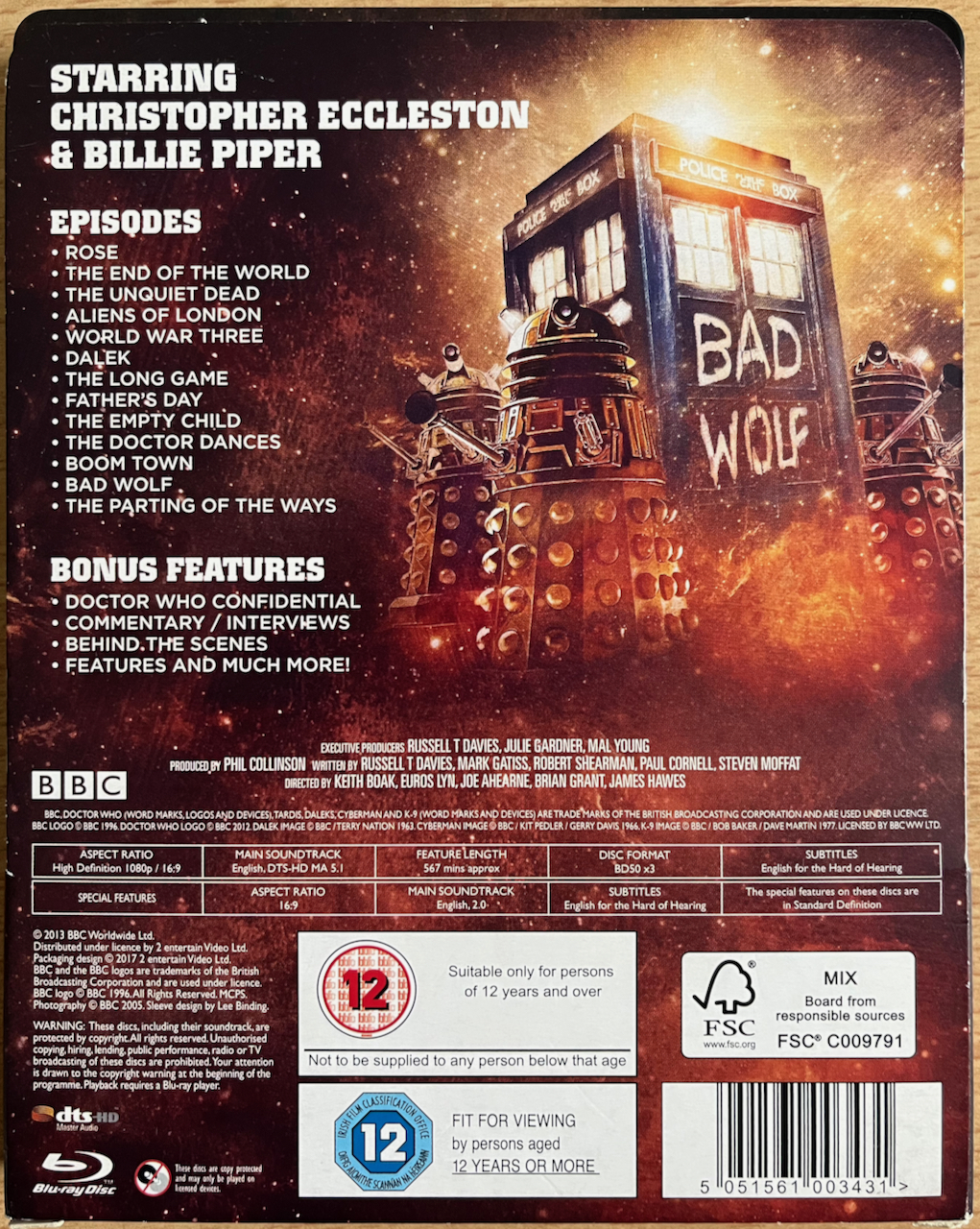 The back of the cardboard sleeve for the Doctor Who Series 1 Blu-ray steelbook, showing the list of episodes and extras, next to a painting of Daleks surrounding the Tardis, which has Bad Wolf painted in large white letters on it.