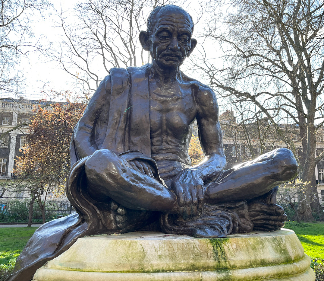 Statue of Mahatma Gandhi sitting in contemplation with his legs crossed.