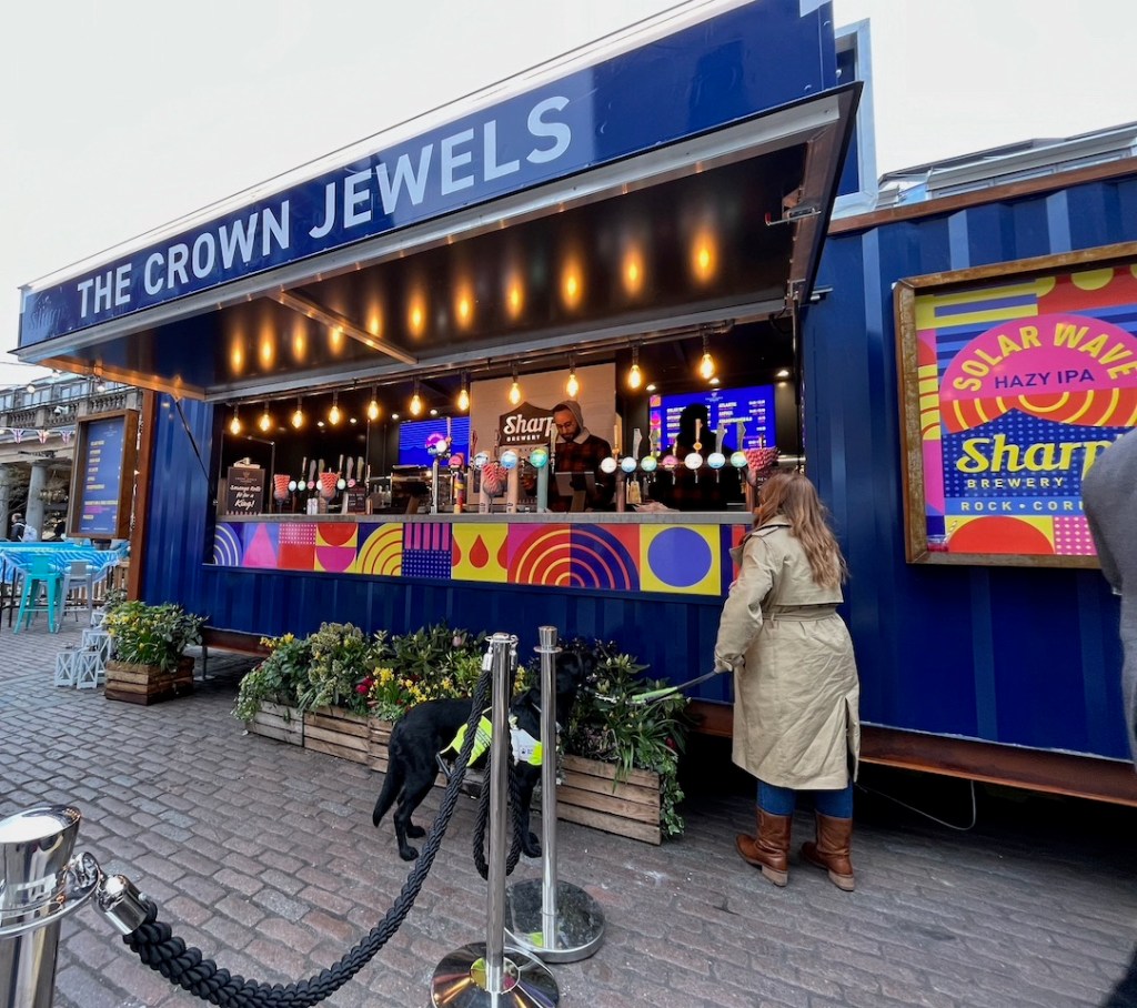 Emily and black guide dog Rosie standing at an outdoor bar called The Crown Jewels in Covent Garden.