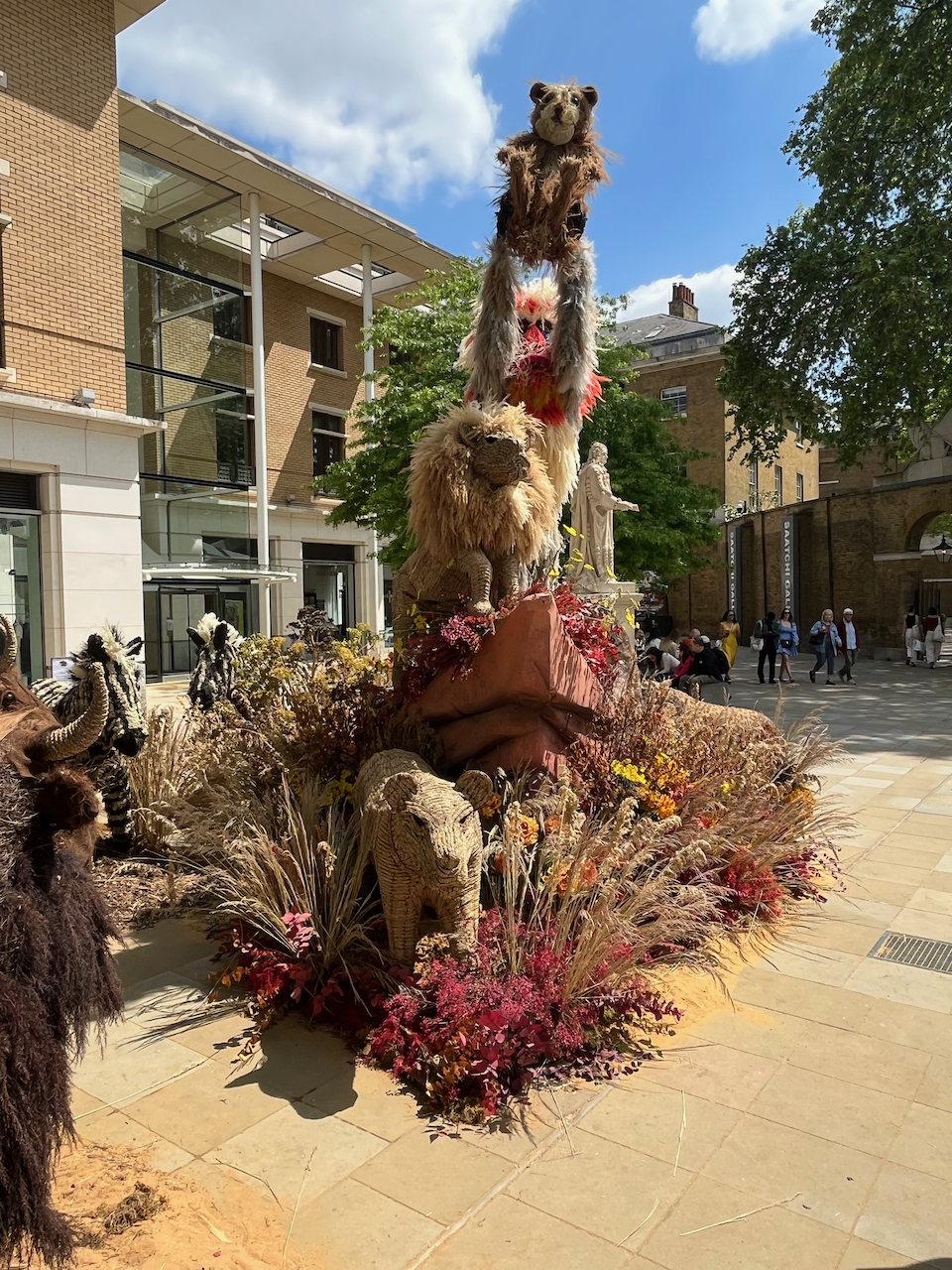 A floral display representing The Lion King, with Rafiki the mandrill holding up Simba the baby lion, while standing on a large rock next to an adult lion.
