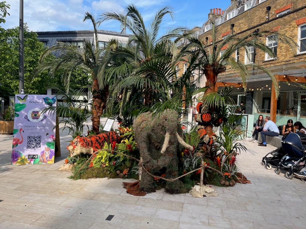 Floral installation of a safari scene, including a grey elephant with big white tusks, an orange and red striped tiger, and some tall leafy trees.