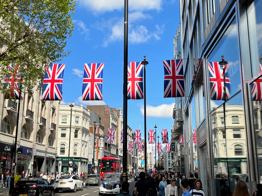 A row of large Union Jack flags hanging across Oxford Street, with several more visible in the distance.