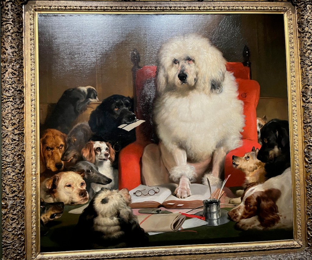 A painting showing a big white fluffy dog standing with his paw on the left page of an open book, while a pair of glasses sits on the right page. A black dog next to it is holding a piece of paper in its mouth, as if wanting to present it to the white dog. Other dogs of various breeds are gathered around, as if waiting for the big white dog to speak to them.