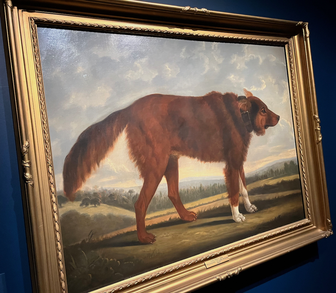 A painting of a large brown dog standing in a field, with trees and hills in the background.