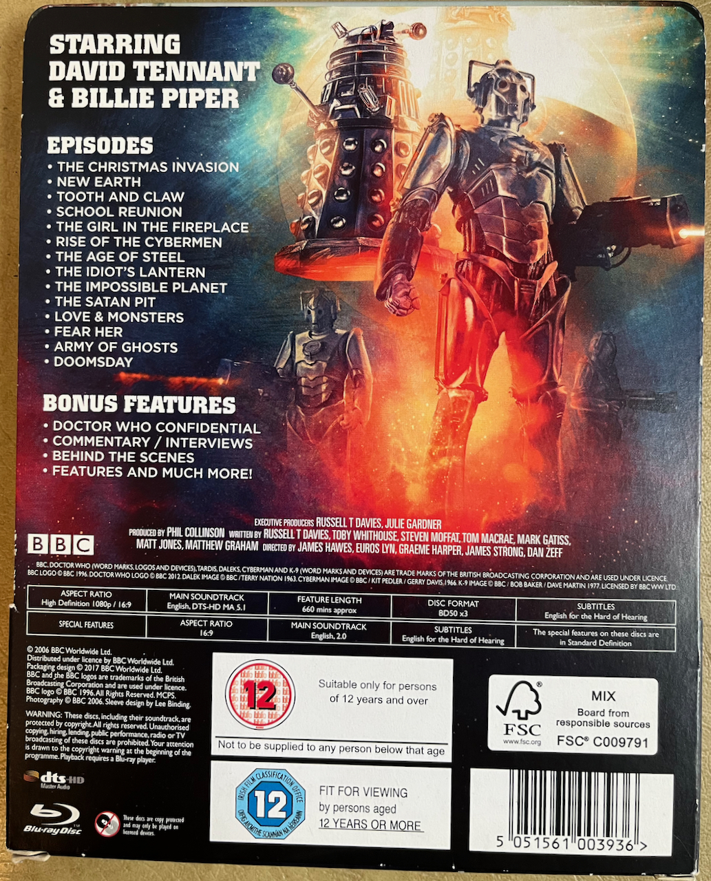 The back cover of the cardboard pocket that houses the Doctor Who Series 2 Blu-ray Steelbook. A list of the episodes and special features sits alongside artwork of Daleks and Cybermen.