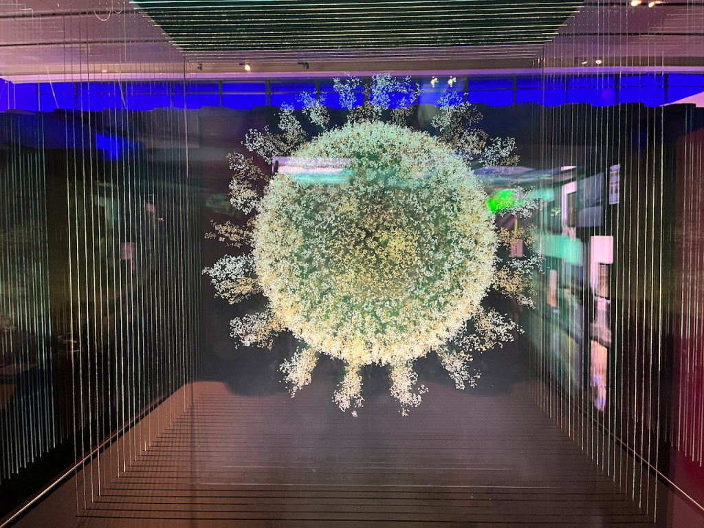 2020: The Sphere That Changed The World by Angela Palmer. This artwork looks like a huge coronavirus particle, a big ball with spikes all over it, floating behind glass.