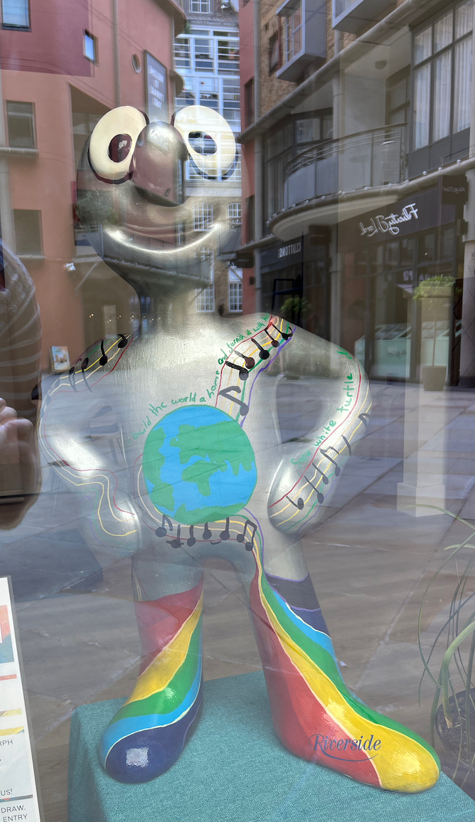 Riverside Spirit, a silver statue of Morph featuring an image of the Earth on his chest with musical notes coming out of it, and rainbow-striped boots on his legs.
