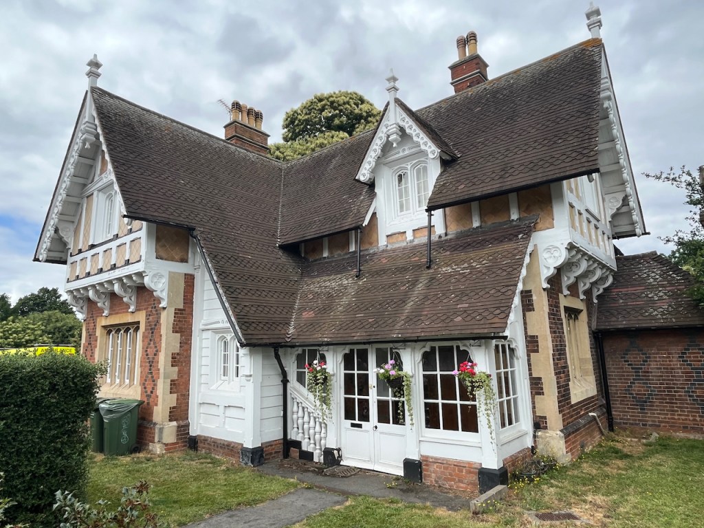 Blackheath Gate Lodge, a Victorian building with Tudor stylings, mainly white but with some light brown elements, and very deep sloping roofs.