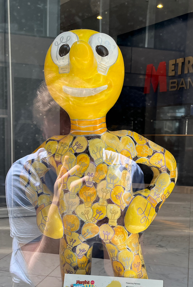 Bright Ideas, a yellow statue of Morph covered in children's drawings of bright lightbulbs. Even his hands and eyes are designed to look like bulbs, and a metallic design around his neck suggests his whole head is a lightbulb.
