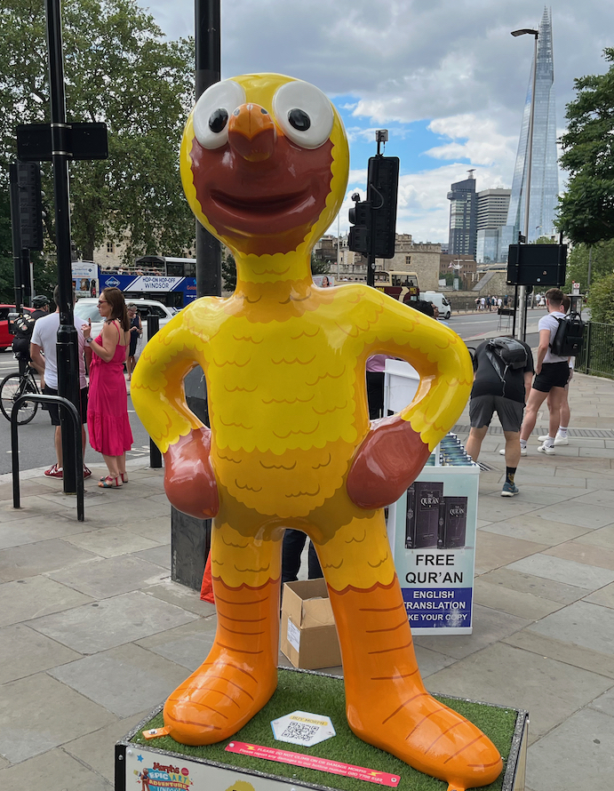 Canary Morph, a statue of Morph with his yellow body covered in wavy lines representing feathers. The face around his mouth and nose is a brown colour, as are his hands, while his lower legs and feet are orange.