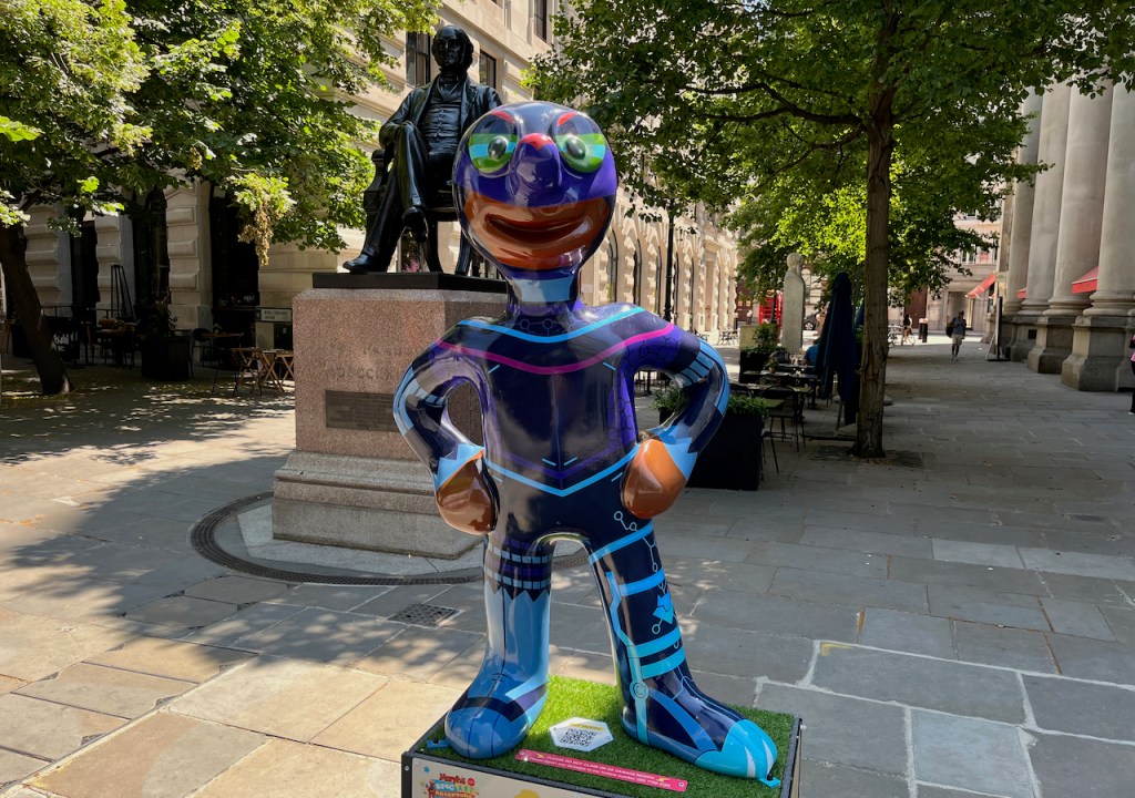 Cyborg Morph, a statue of Morph whose mouth is visible through a navy suit that covers the rest of his head and body, and is decorated with light blue and dark pink lines and patterns, making him look a bit like a robotic version of himself.