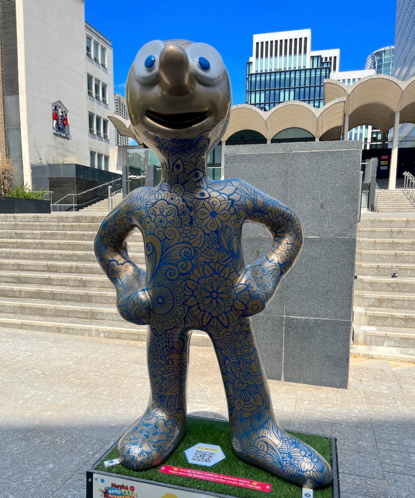 Diverse-city, a statue of Morph whose silver body is covered with a myriad of blue drawings of flowers and swirling patterns.