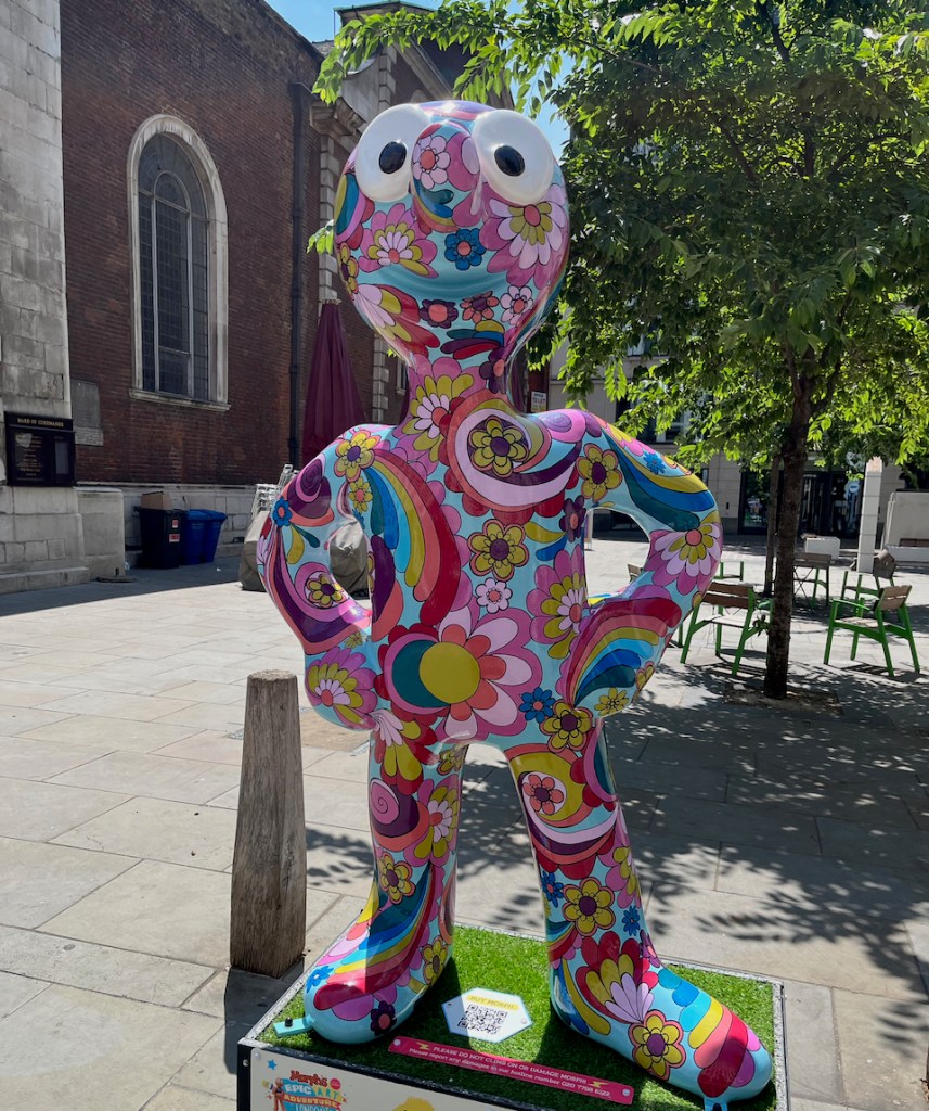 Good Vibes, a statue of Morph covered in a colourful psychedelic mixture of swirling rainbows, flowers and other patterns.