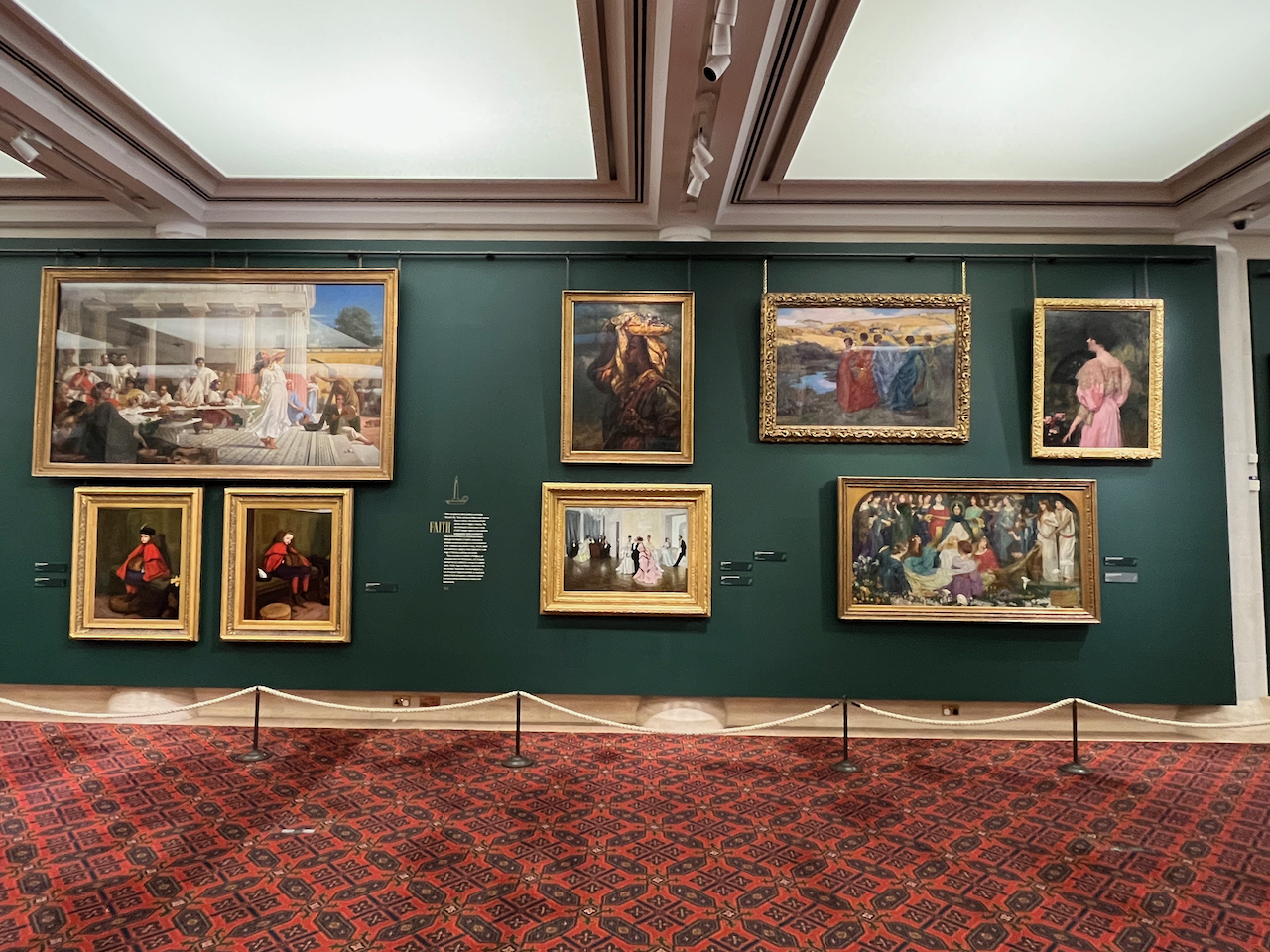 Paintings of various people, mainly female, on the wall of the Victorian gallery in the Guildhall Art Gallery, including a pair of pictures showing a child sitting on a pew in church, one of her looking enthusiastic and the other looking less interested.