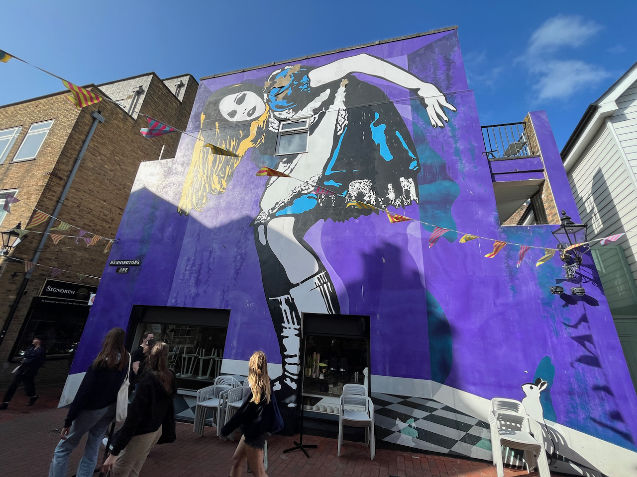 A mural of a woman who fills the entire wall of a large building. Standing side-on to us, and with her face turned towards us so her long blonde hair falls behind her, she is bending over in what appears to be a maid's outfit, with a white apron over the shiny black material, and her bottom is pressing against a wall behind her. Despite how that description might sound, the image is tasteful and doesn't reveal anything inappropriate.