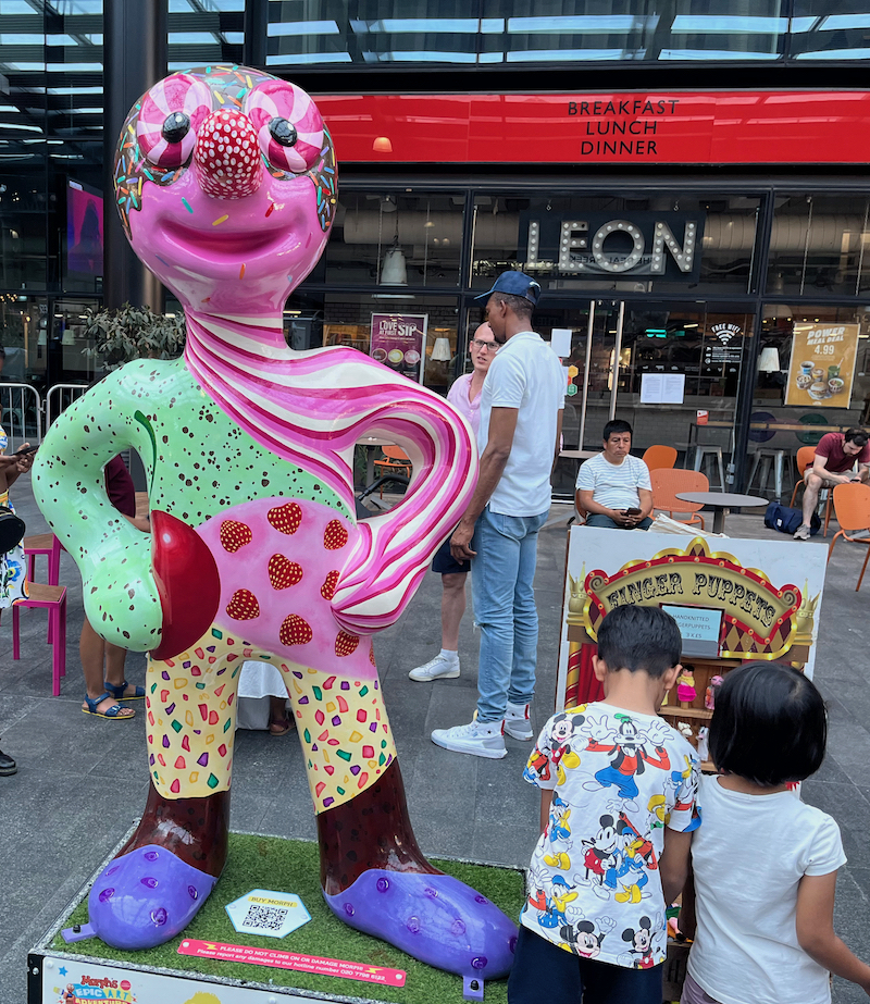 Mmmmmmmm-morph, a statue of Morph decorated like an ice cream sundae, including green mint chocolate chip, pink and white raspberry ripple, red strawberries, chocolate, blueberries and sprinkles, and a cherry in his hand.