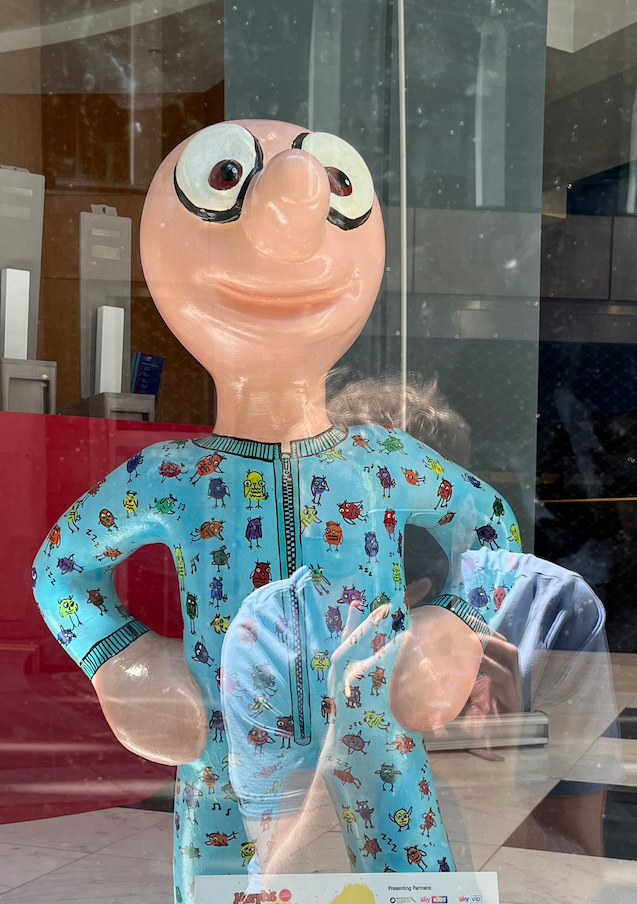 Morley the Morph - Ready to Board, a statue of Morph wearing a light blue onesie with a zip down the middle, covered in lots of colourful child's drawings of small owls.