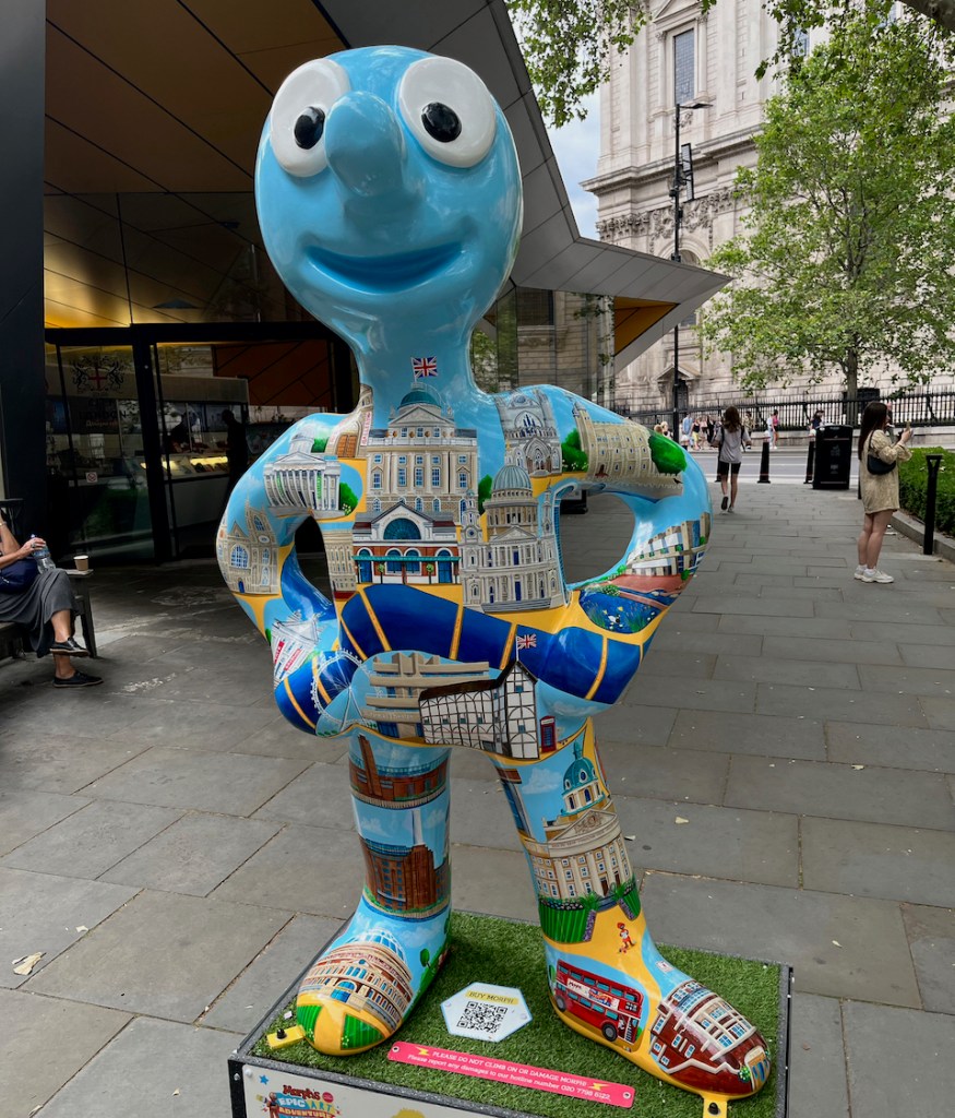 Morph and Friends Explore London, a statue of Morph in light blue, covered in imagery of famous London sights, including the River Thames, the Bank of England, Buckingham Palace, the London Transport Museum, St Paul's Cathedral, Westminster Abbey, the Tower of London, the London Eye, Shakespeare's Globe, Tate Modern, Battersea Power Station, the Royal Albert Hall, Imperial War Museum, a red telephone box and a red double decker bus.