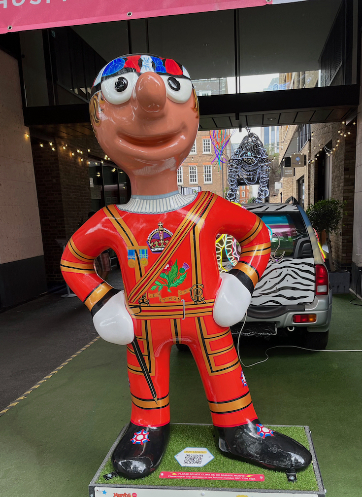 Morph the Yeoman Guard, a statue of Morph wearing a red Beefeater's outfit with gold detailing and an image of a crown, plus a red, white and blue cap on his head.