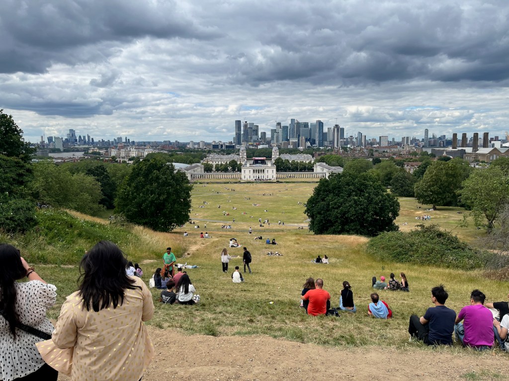 View from the hill by the Royal Observatory, looking over a massive expanse of grass and trees towards the Queen's House building at the end of the park, and the London skyline behind it.