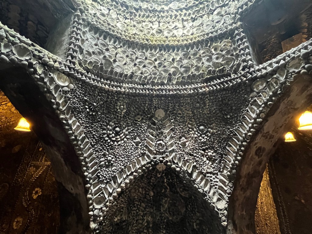 A curved wall decorated with lots of shells, forming arches beneath.