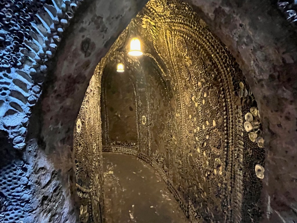 A narrow corridor with intricate patterns made of shells on the walls, and a couple of small lights hanging from the ceiling.