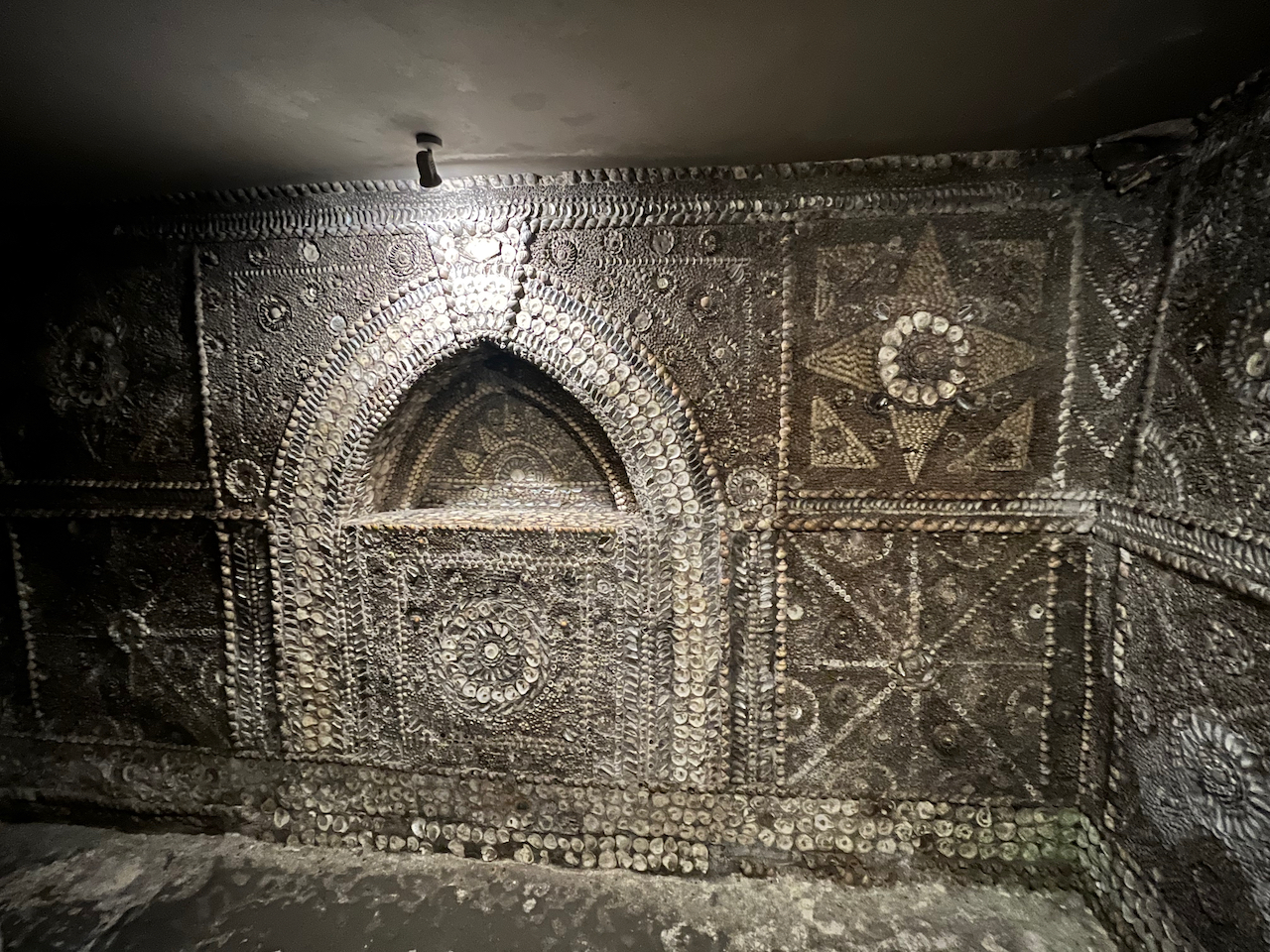 An altar room with ornate shell patterns on the walls, including around the border of an arched recess in the wall.