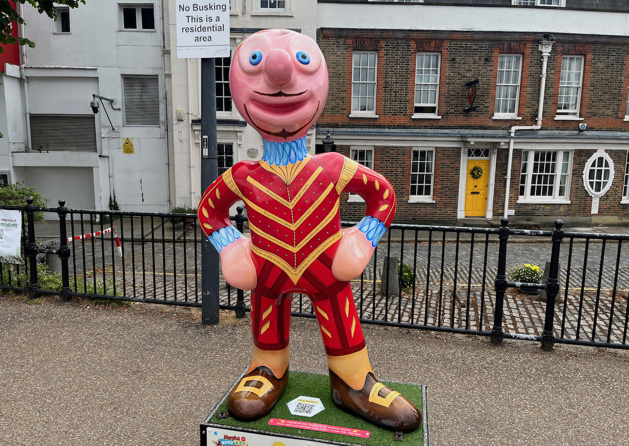 The Bard, a statue of Morph wearing a red jacket and trousers with gold stripes and gold trim, a blue ruff around his neck, brown shoes with gold buckles, and on his face he has a very thin black beard and moustache.
