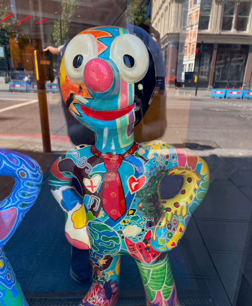 This Is Us, a mini statue of Morph, who is covered in all sorts of random colourful shapes and patterns, including a red tie around his neck, musical notes, hearts, the globe and flowers.