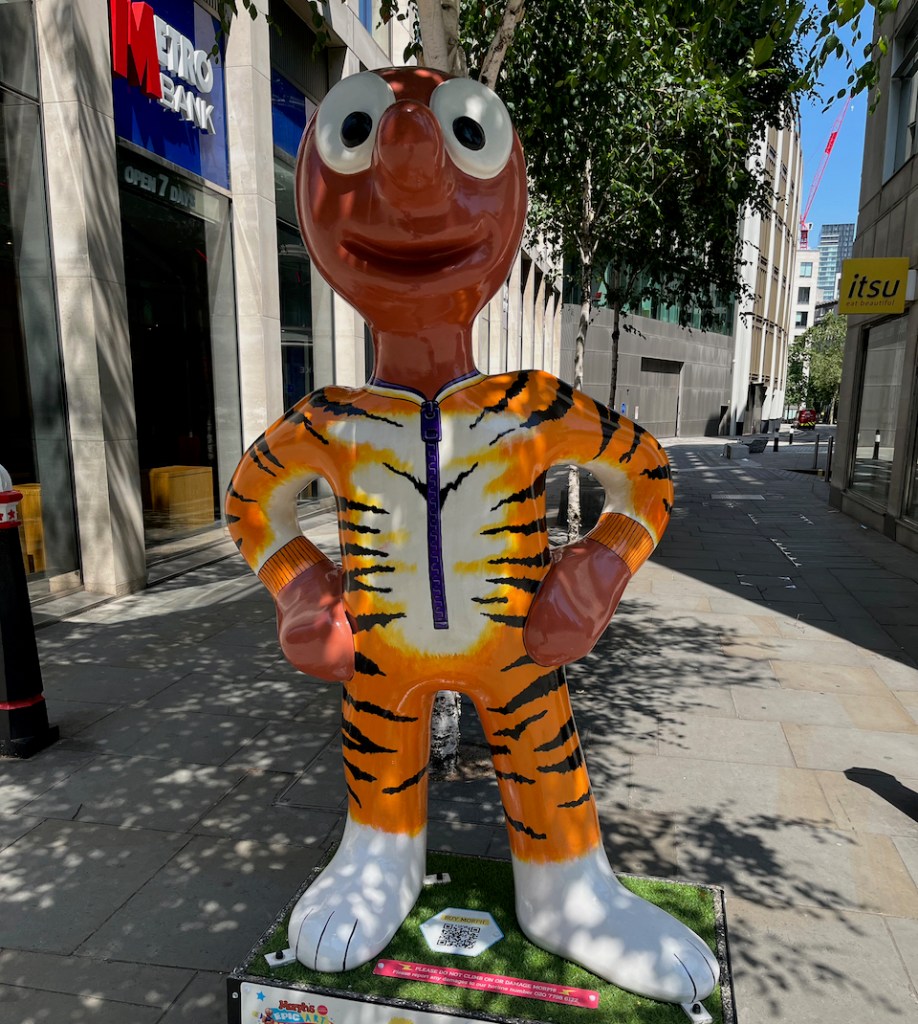 Tiger Morph, a statue of Morph wearing a tiger onesie, with black stripes, a white chest and white feet. The onesie has a long zip down the middle of it.