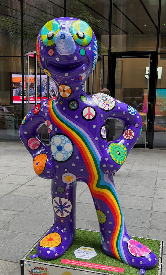 Wheelie, a statue of Morph whose dark blue body has a rainbow snaking from his right shoulder down to his left foot, while the rest of the space is covered by a variety of colourful circular patterns and white polka dots.