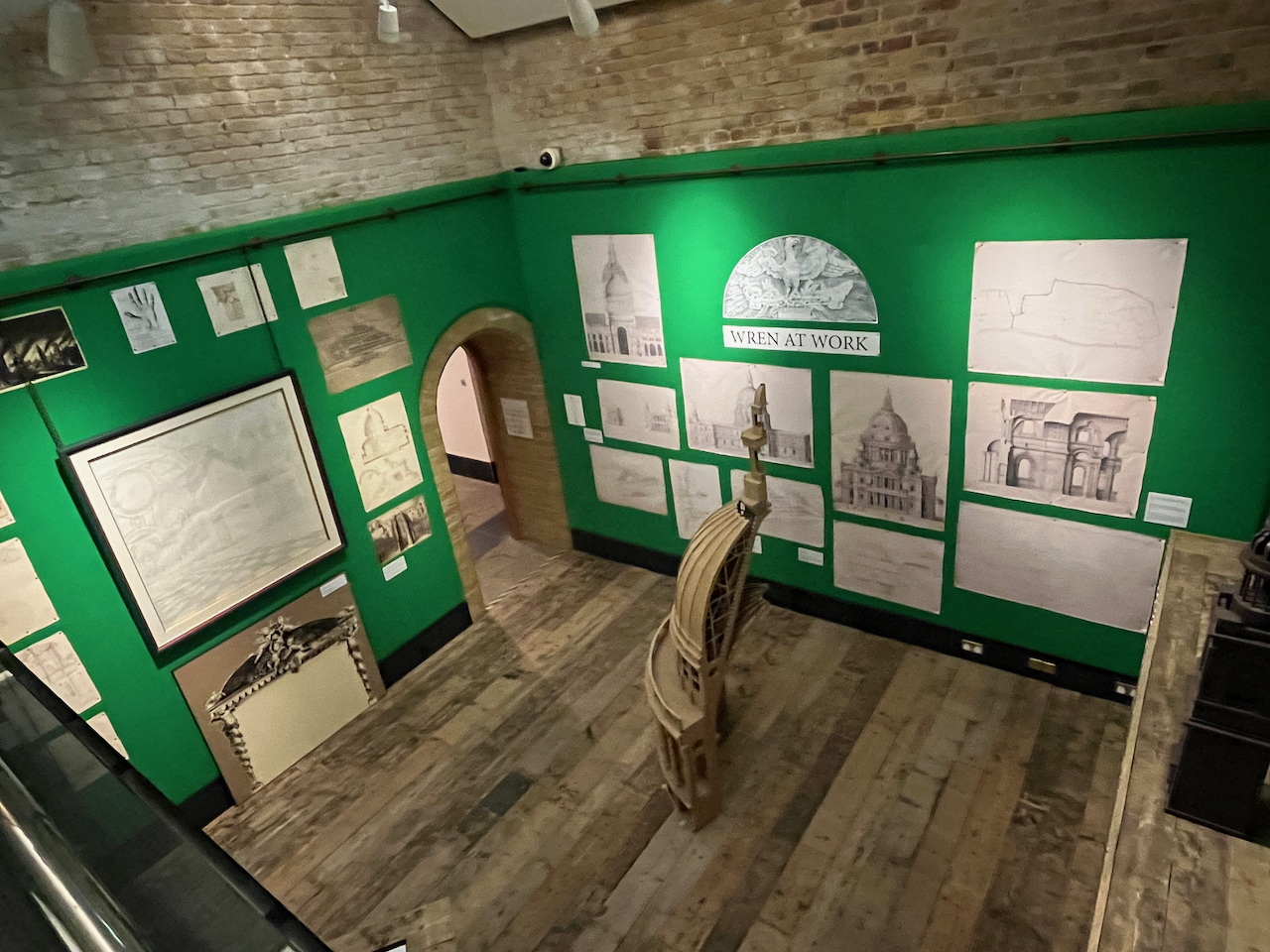 Overhead view of a gallery called Wren At Work, with sketches by Christopher Wren on the walls, and a model of the dome of St Paul's Cathedral cut in half on the floor.