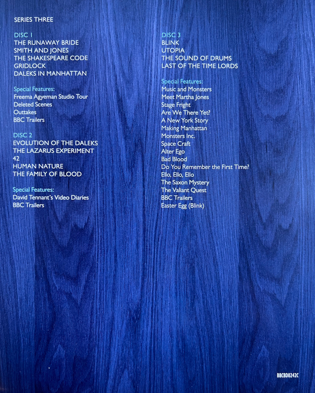Rear side of the flyer included with the Doctor Who Series 3 Blu-ray Steelbook, showing the list of episodes and extras on each of the 3 discs, in white text over a close-up of the blue wood that makes up the exterior of the Tardis.