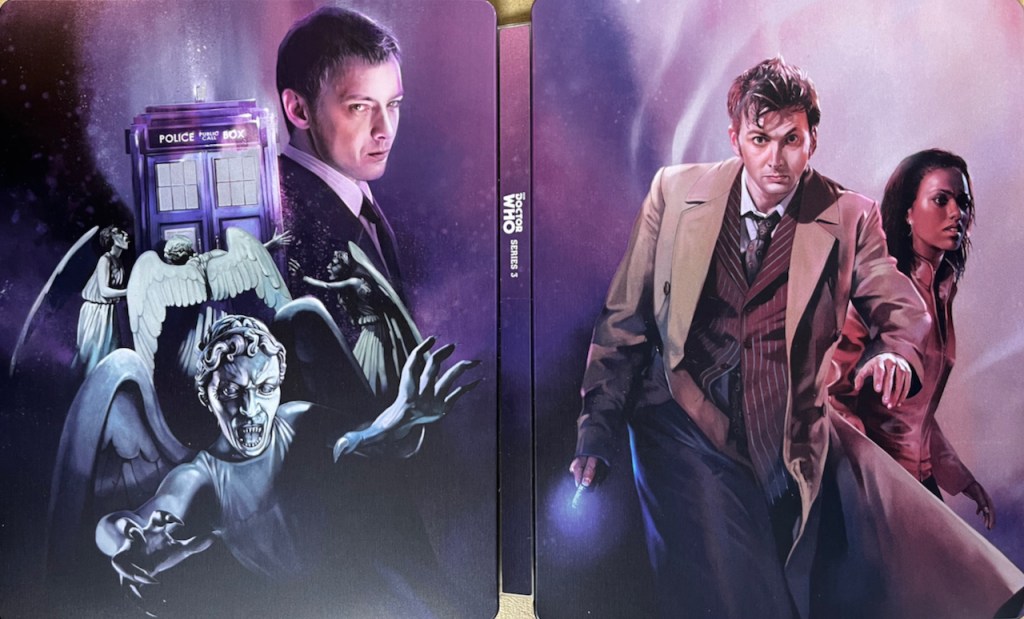 The full cover spread artwork for the Doctor Who Series 3 Blu-ray steelbook. The front cover shows David Tennant as the Doctor, wearing a light brown jacket over a pinstripe suit as he strides forward with his sonic screwdriver in his right hand and a serious, determined expression on his face. Martha Jones is behind him wearing a red leather jacket and glancing fearfully to the side. Meanwhile the back cover shows John Simm as The Master, watching over a group of Weeping Angels surrounding the Tardis, while another Weeping Angel is flying towards us with its teeth bared angrily, its arms outstretched as if to grab us.