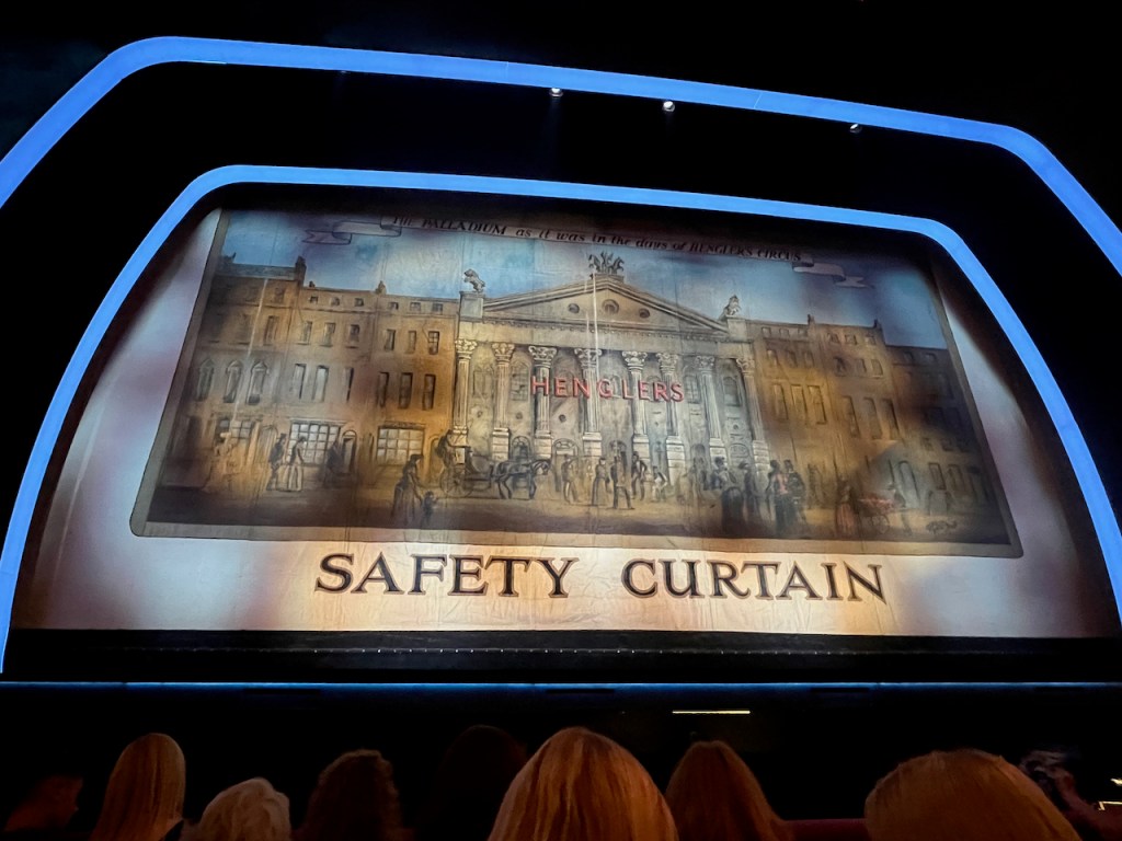 The safety curtain at the Palladium, showing a very old picture of the theatre with people gathered outside. Text at the very top reads The Palladium as it was in the days of Hengler's Circus, while the word Henglers appears in large red letters across the front of the Palladium building.
