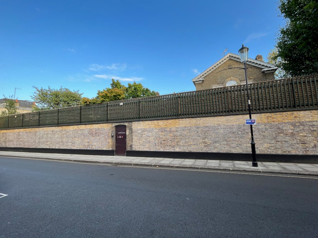Garden Lodge, Freddie Mercury's former home. The top of the house is only just visible above the security fence lined with razor wire, on top of the tall brick wall surrounding the premises.