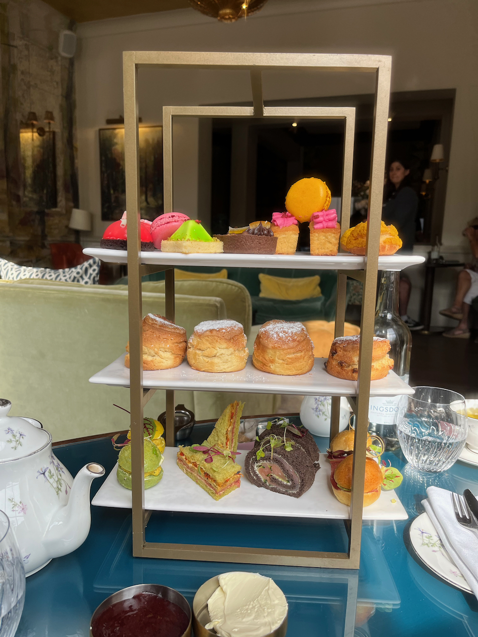 A rack of afternoon tea goodies, with sandwiches on the bottom, scones in the middle and patisserie items on the top shelf.