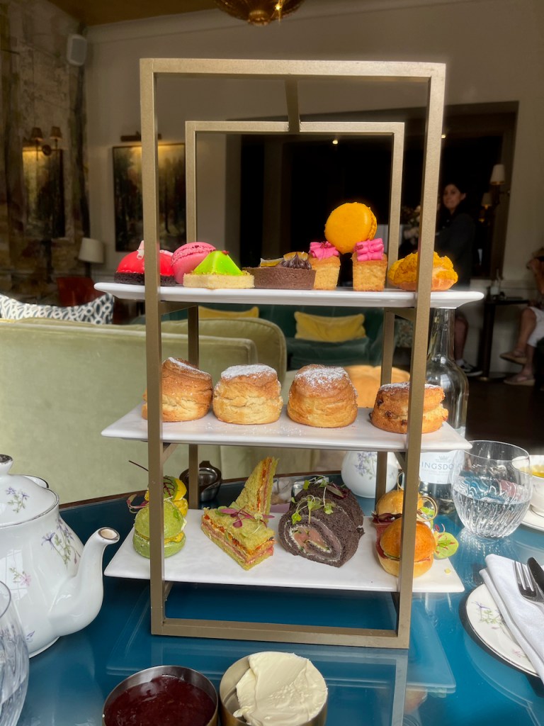 A rack of afternoon tea goodies, with sandwiches on the bottom, scones in the middle and patisserie items on the top shelf.