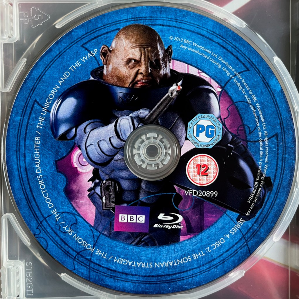 Disc 2 in the Doctor Who Series 4 Blu-ray set. It features a photo of Sontaran General Staal, whose bald head pokes out of the top of his dark blue armour as he points a sharp instrument out in front of him with an angry look on his face. A blue border around the edge of the disc contains the episode names and copyright information.