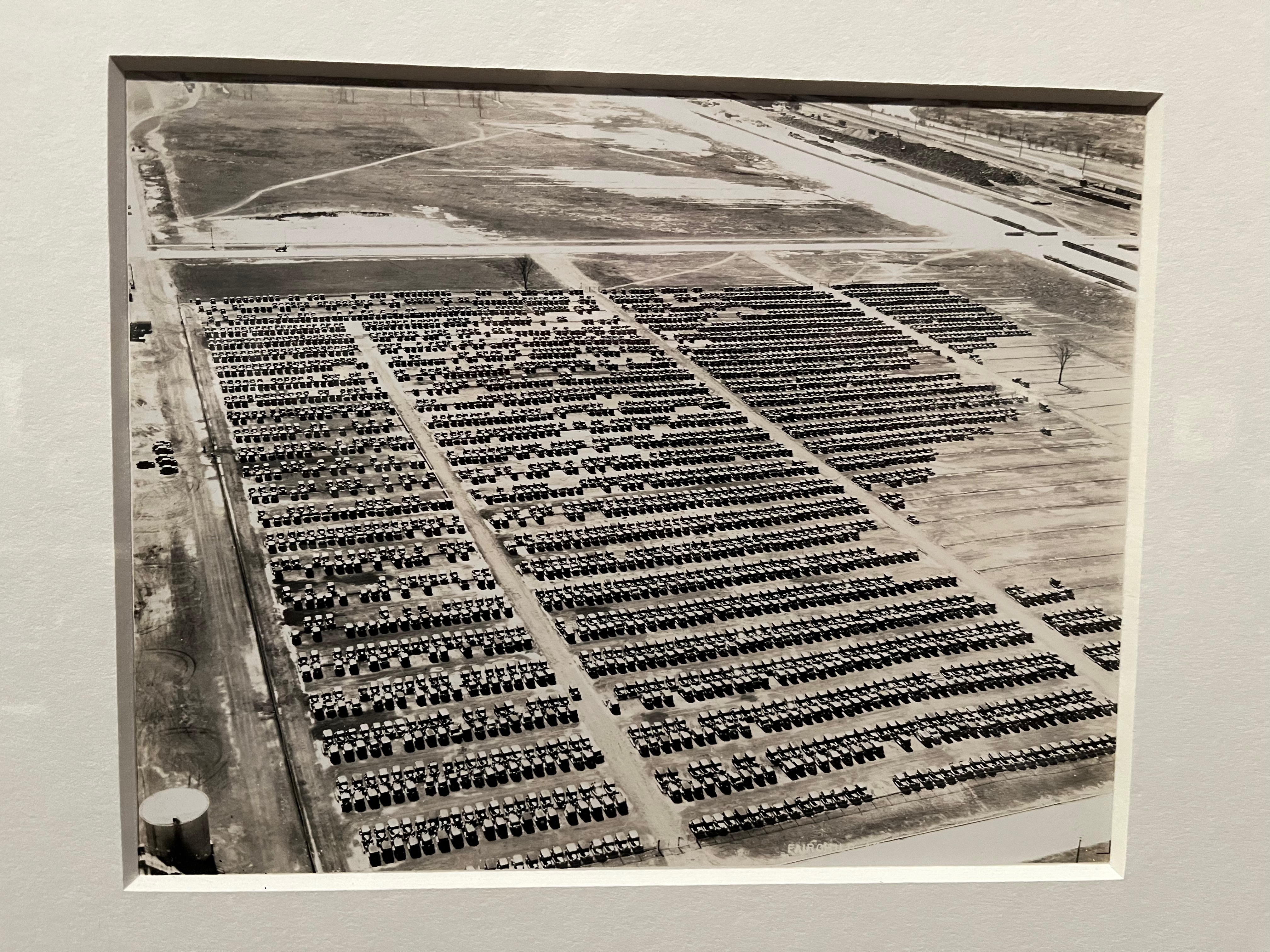 Black and white photo by showing an aerial view of thousands of cars parked in rows at the Ford Headquarters in Michigan in 1936.