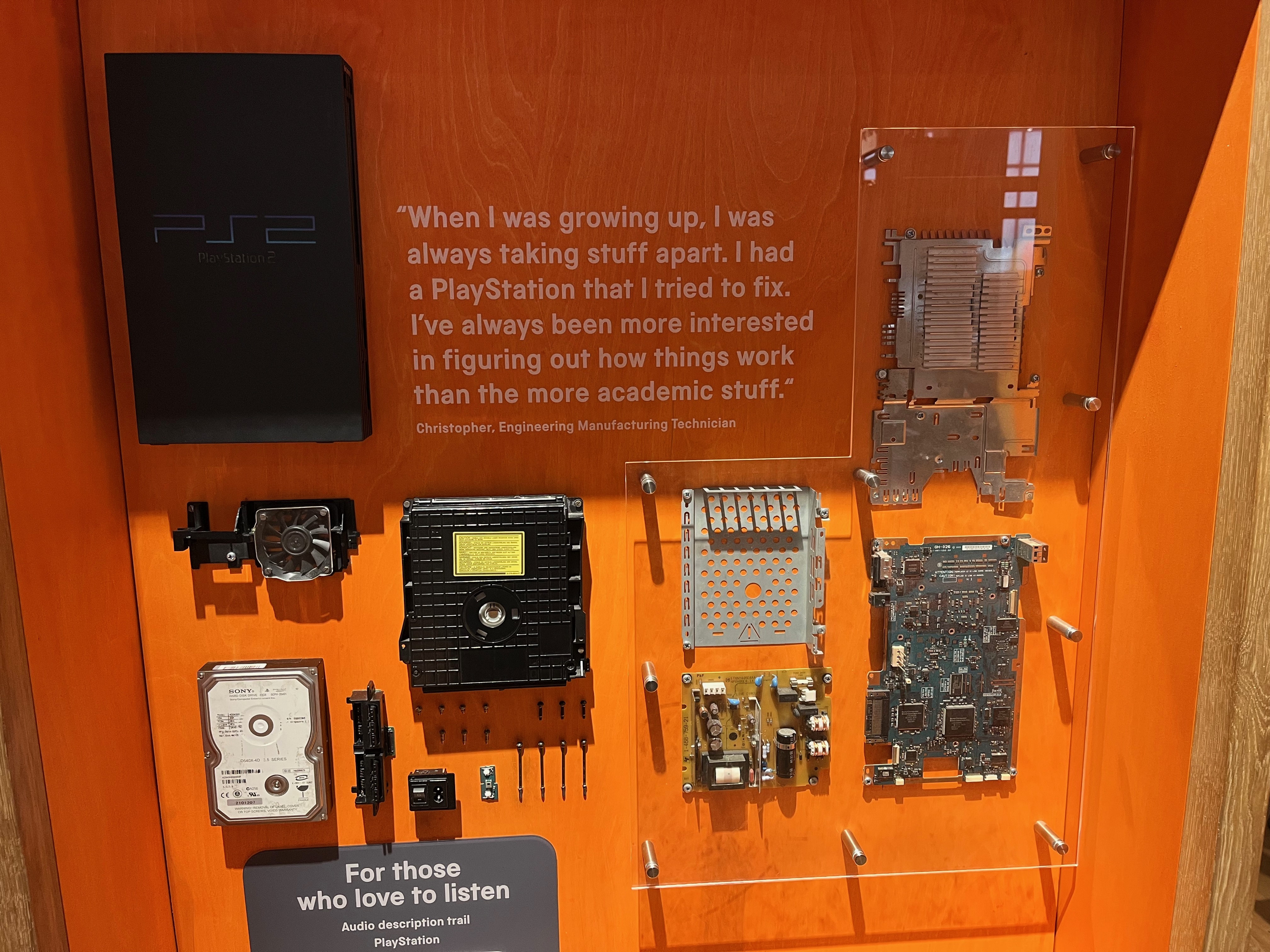 A PlayStation 2 console that has been broken down into its individual components, arranged for people to touch in an orange display case. A quote from Christopher, an engineering manufacturing technician, is shown in large white text in a space amongst the various items. He says When I was growing up, I was always taking stuff apart. I had a PlayStation that I tried to fix.
I've always been more interested in figuring out how things work than the more academic stuff.