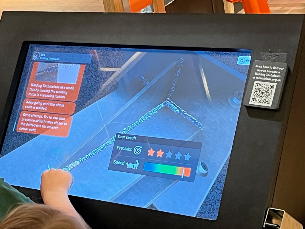 A interactive touch screen with a welding demonstration, where the player is trying to use a welding torch on a piece of metal, and they are marked on precision and speed.