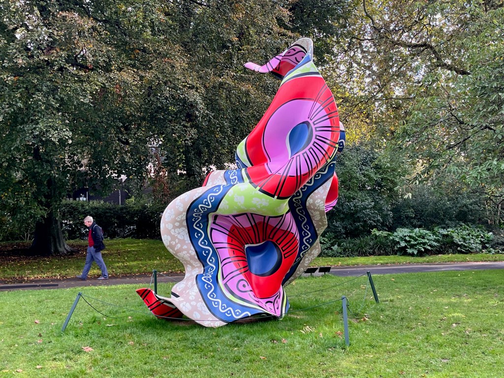 A sculpture by Yinka Shonibar called Material (SG) 4, which looks like a huge piece of fabric caught in a strong wind, covered in a myriad of bright and bold coloured patterns.