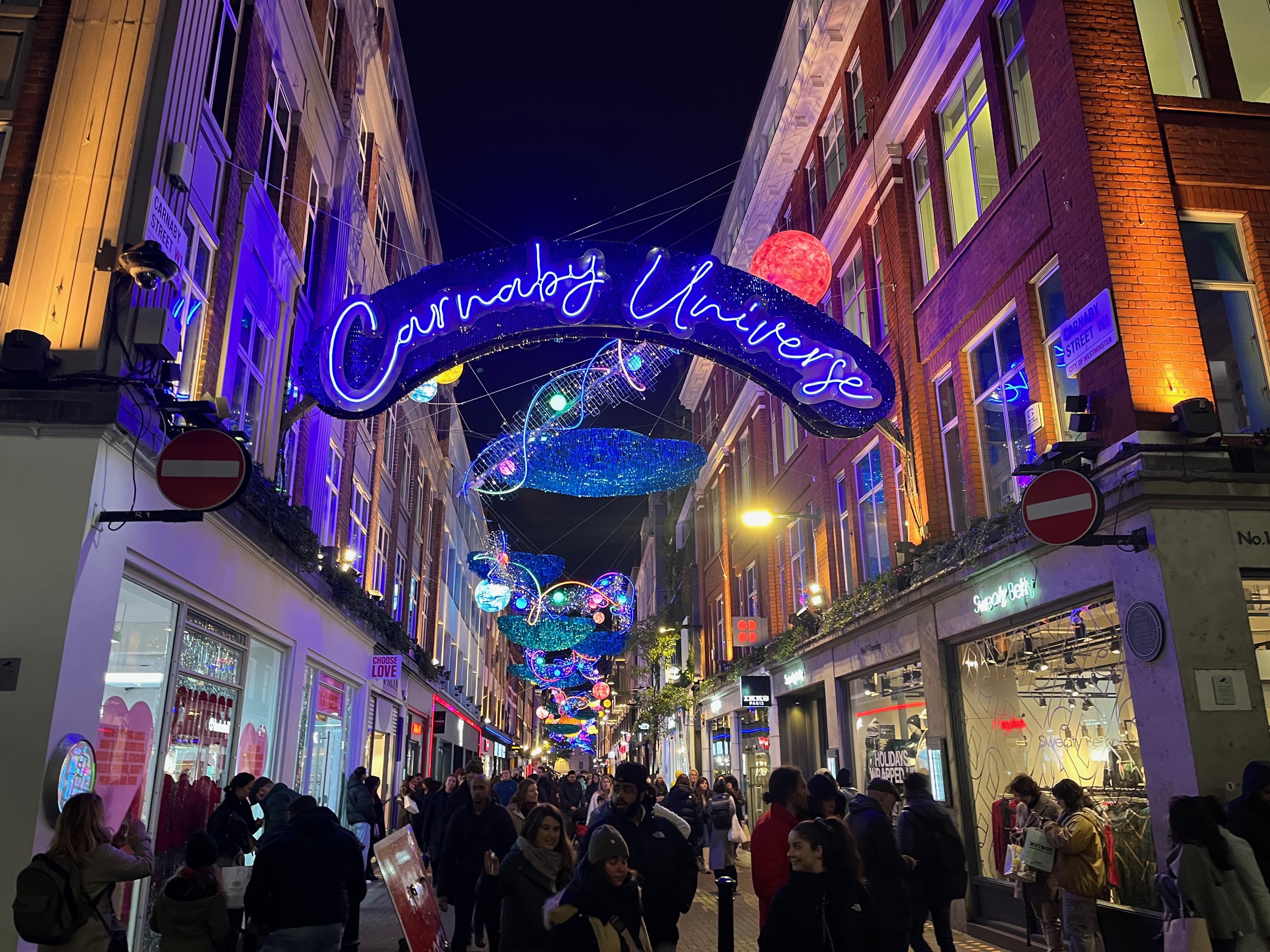 An archway over the entrance to Carnaby Street, on which the words Carnaby Universe are written in bright blue neon letters.